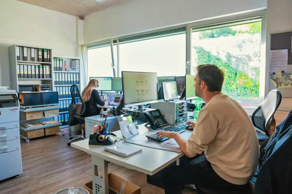 Zwei Mitarbeitende an ihren Arbeitsplätzen im Büro in Korb
