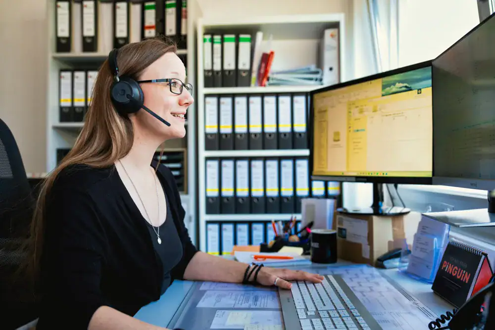 Mitarbeiterin mit Headset am Schreibtisch im Büro in Korb